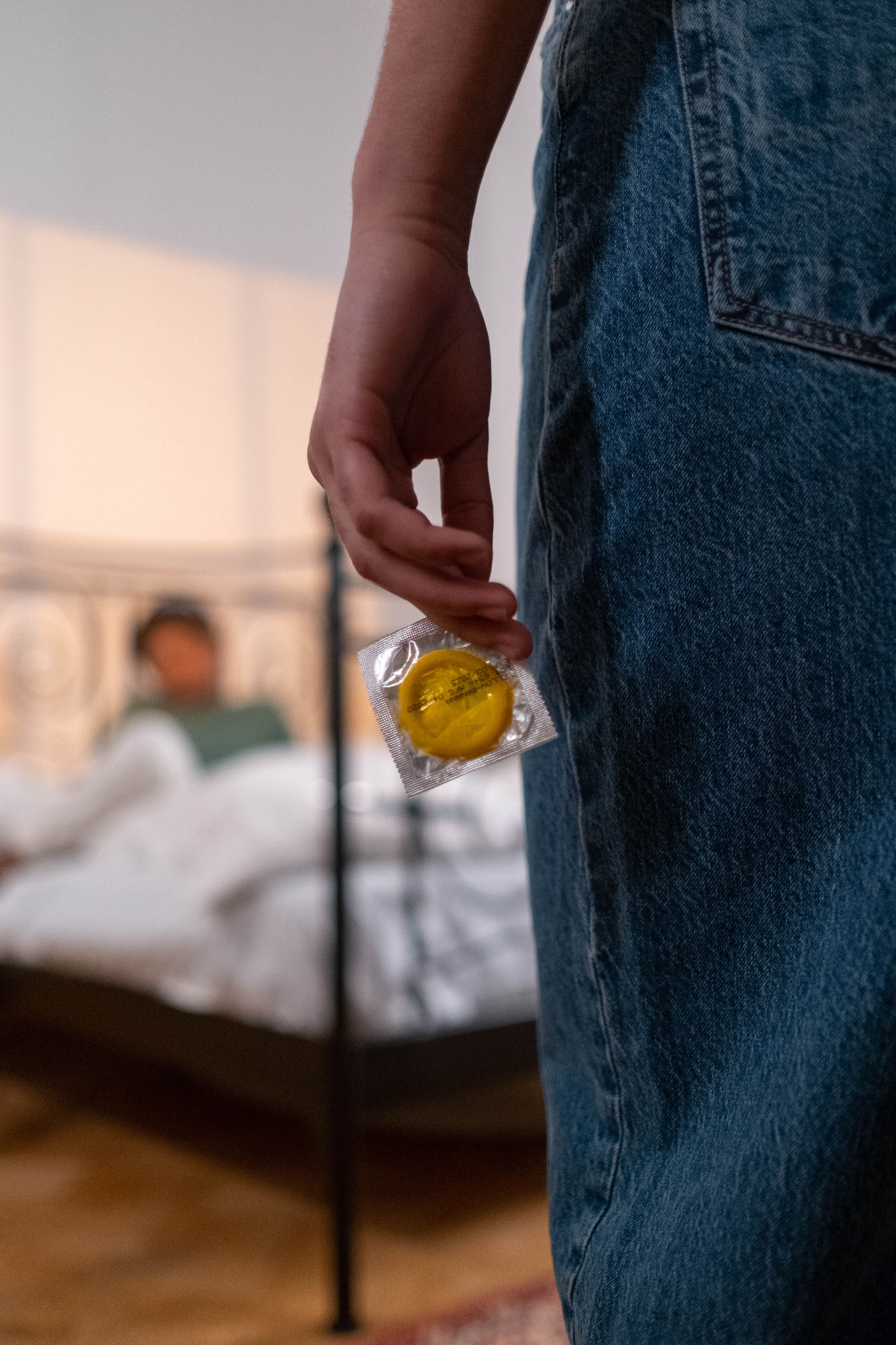A person holding a condom behind their back in an intimate setting