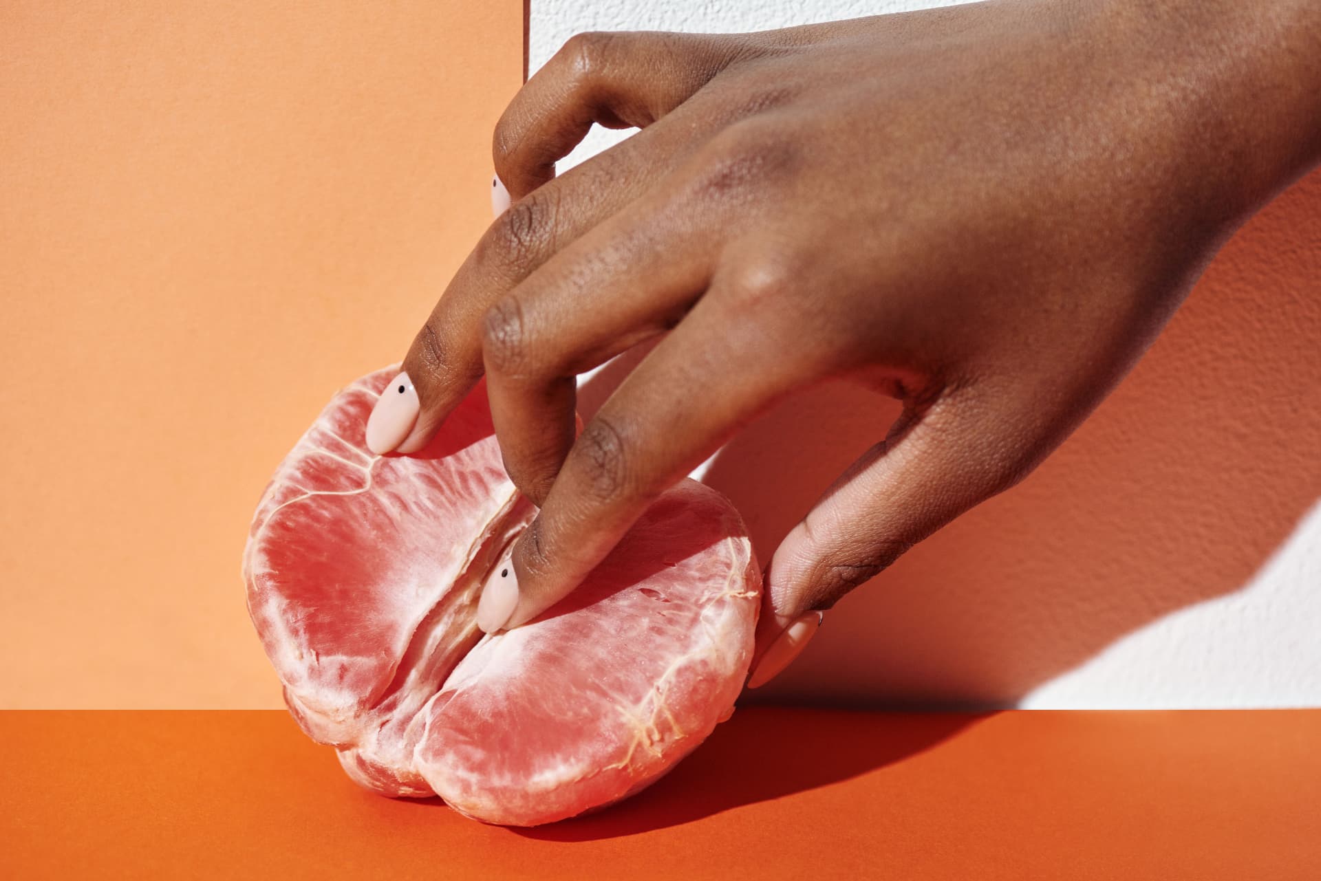 A hand gently touching a citrus fruit against a warm orange background